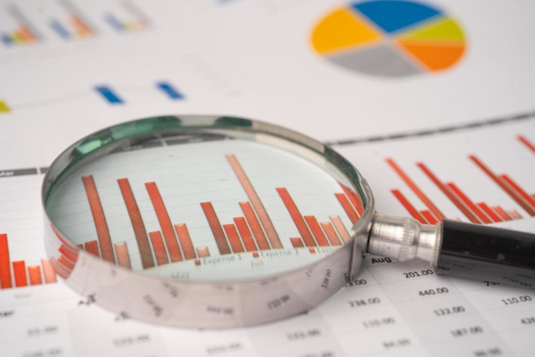 A magnifying glass placed on a stack of financial charts and reports, representing the concept of value investing tips.